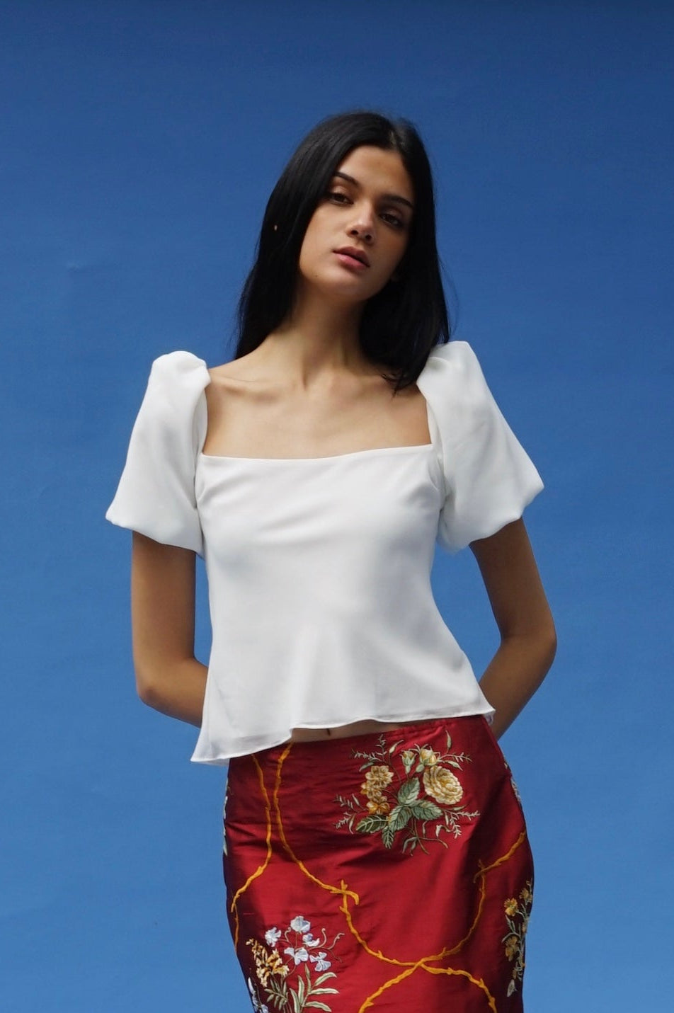 Woman wearing a white top and red floral skirt on a blue background